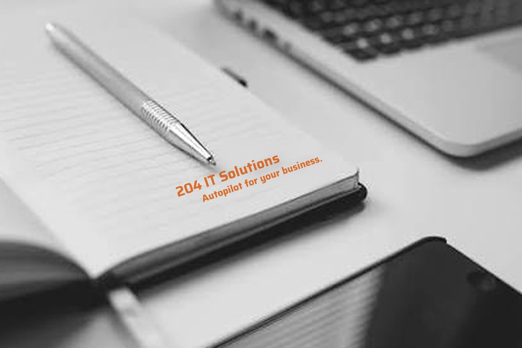 Notebook printed with "204 IT Solutions: Autopilot for your business", beside a pen, laptop and phone